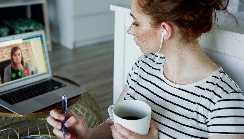 Une femme se formant à distance depuis chez elle avec une tasse de café à la main